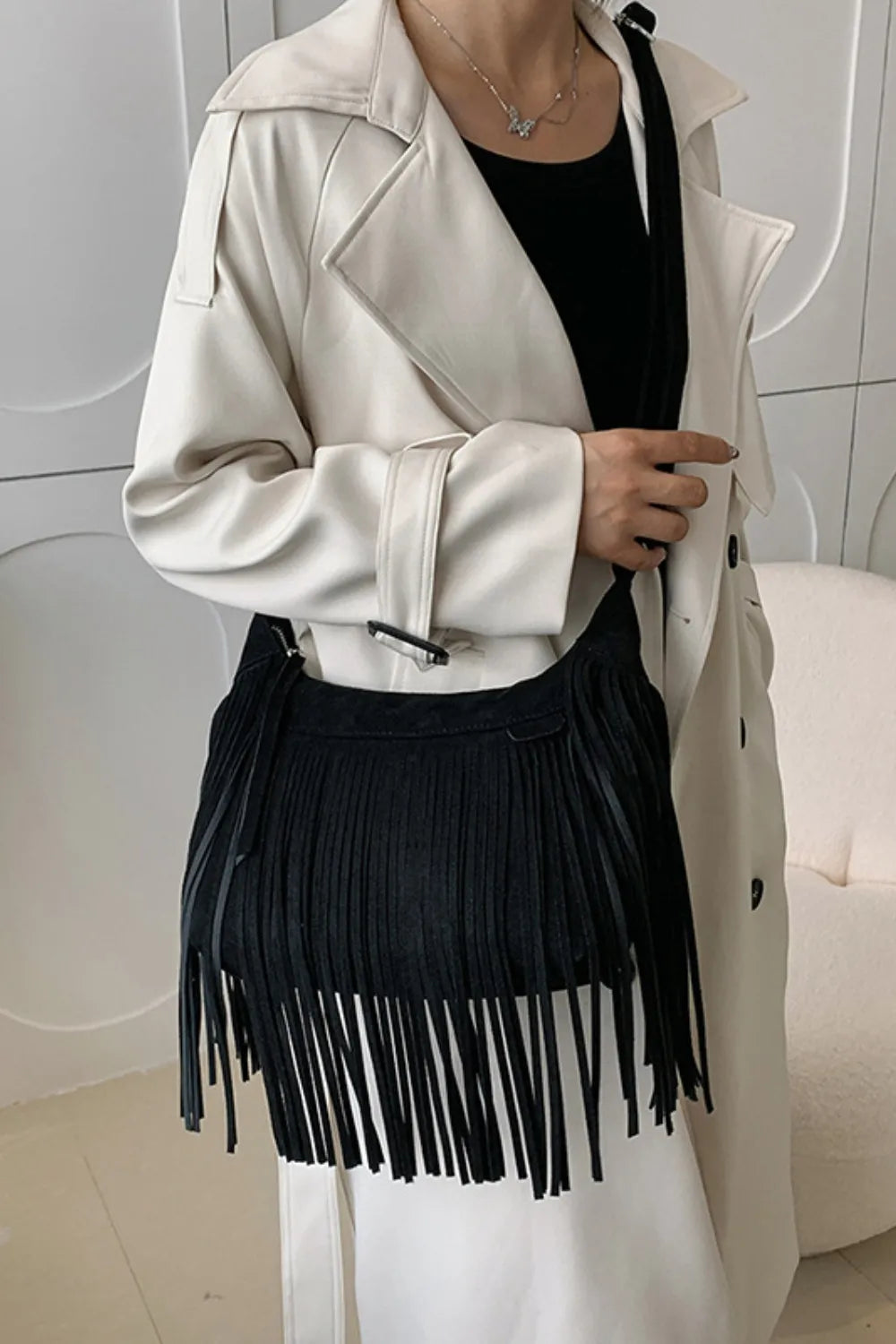 Suede Fringe Adjustable Strap Shoulder Bag worn with a trench coat, showcasing trendy fringe detail and adjustable strap in black.