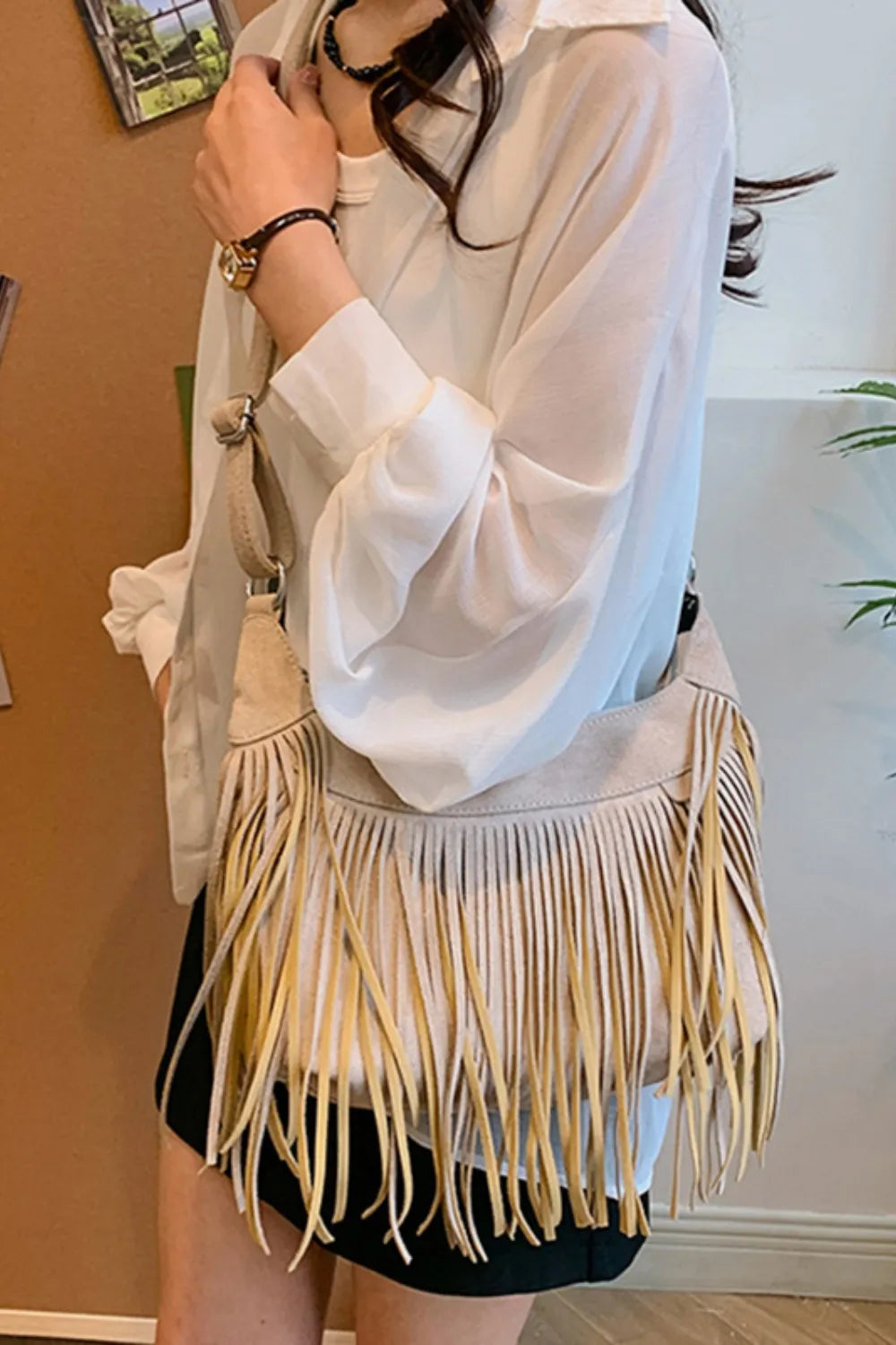 Model showcasing a Suede Fringe Adjustable Strap Shoulder Bag with long fringes, worn crossbody over a white blouse.